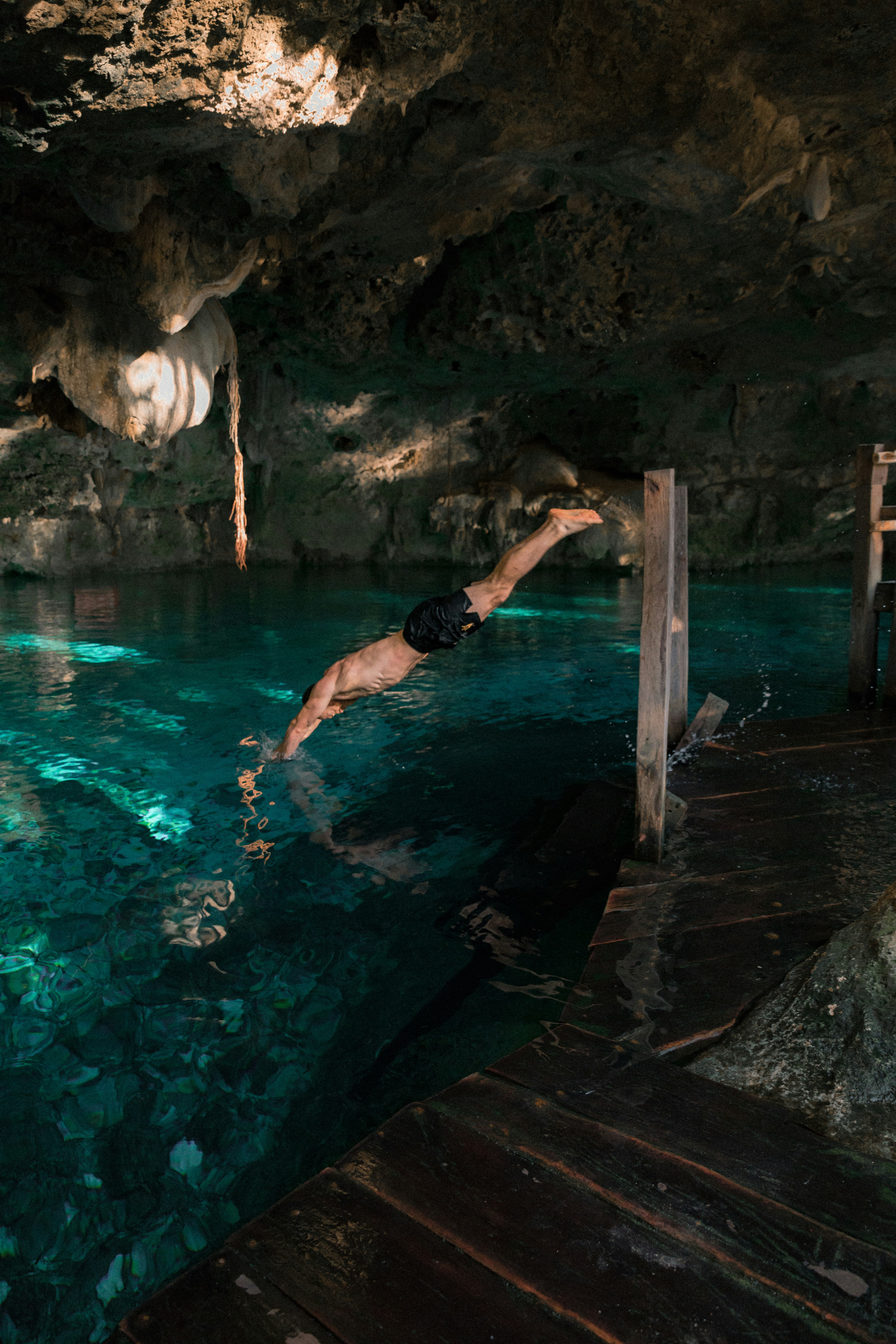 man diving in green underground river water